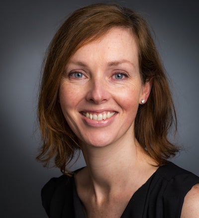 Headshot of Fiona Fennessy wearing a navy sleeveless shirt in front of blue/grey background.