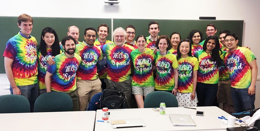 Thomas Michel and MoD boot camp participants are huddled together for a group photo in tie dye T-shirts in a classroom.