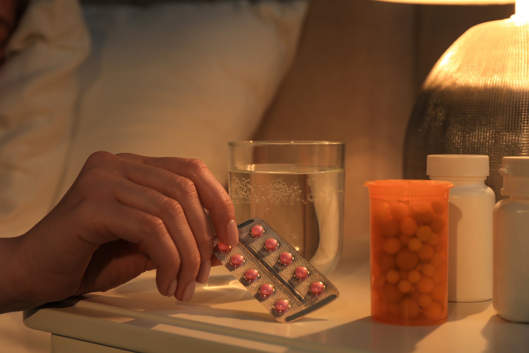 Woman's hand taking pills from bedside table.